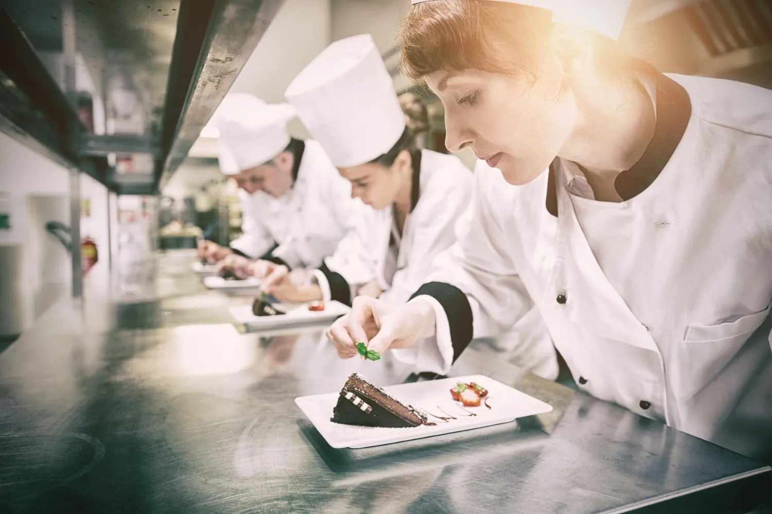 Flow in Commercial Kitchen Design - Chefs standing in a row garnishing dessert plates.